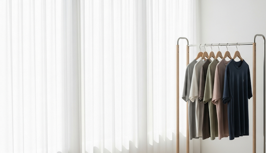 Minimalist and bright background for a t-shirt blog. It shows a modern style coat rack with several t-shirts in neutral colours hung in an orderly fashion. The atmosphere is professional and is illuminated with soft light, without people.