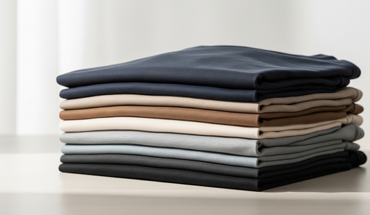 Clean and modern background for a sales blog. It shows a pile of softly coloured T-shirts, perfectly folded on a light wooden surface. The scene conveys quality and order, without people.